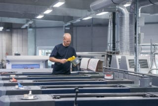 Mitarbeiter streicht beim Bogen-Offsetdruck den Drucker mit Farbe ein in der Druckerei von Stern'sche    